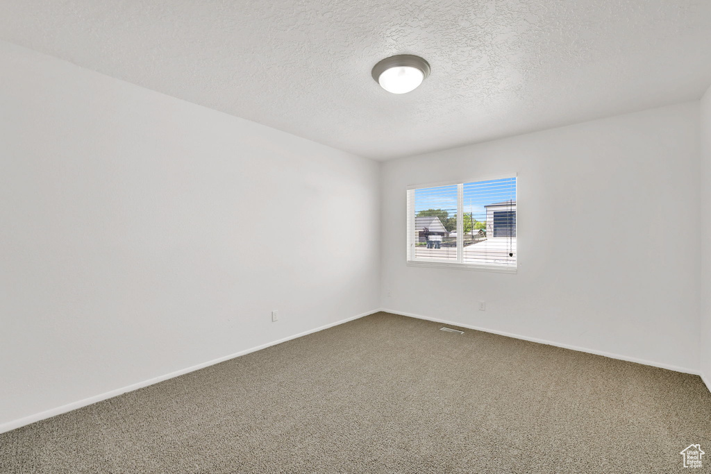 Empty room with dark colored carpet, a textured ceiling, and baseboards