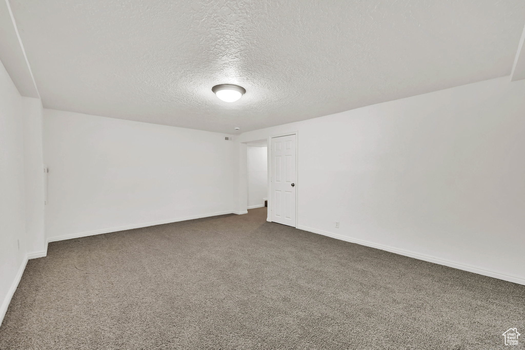 Spare room with dark colored carpet, a textured ceiling, and baseboards