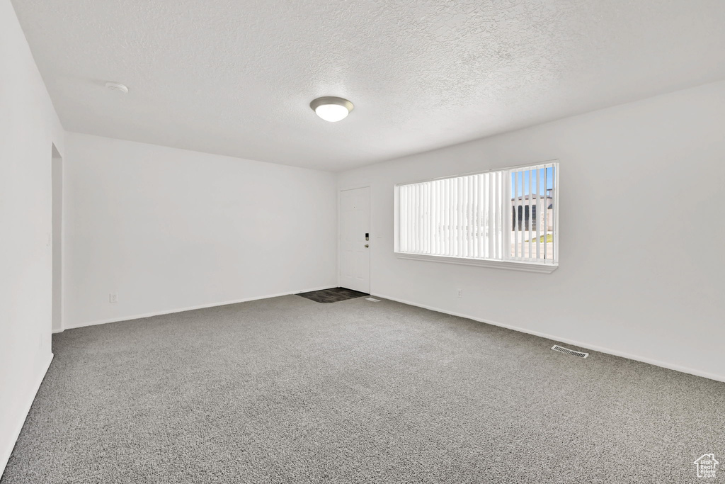 Empty room with a textured ceiling, carpet flooring, and baseboards