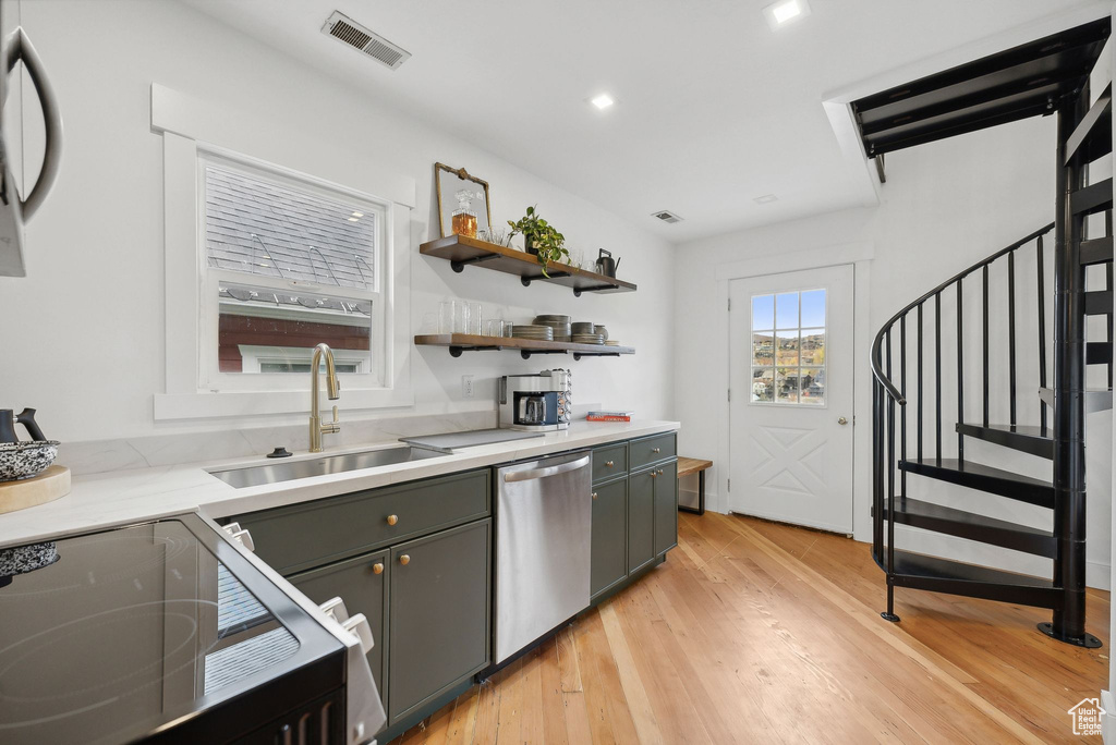 Kitchen featuring stainless steel dishwasher, a sink, light wood-type flooring, open shelves, and stove