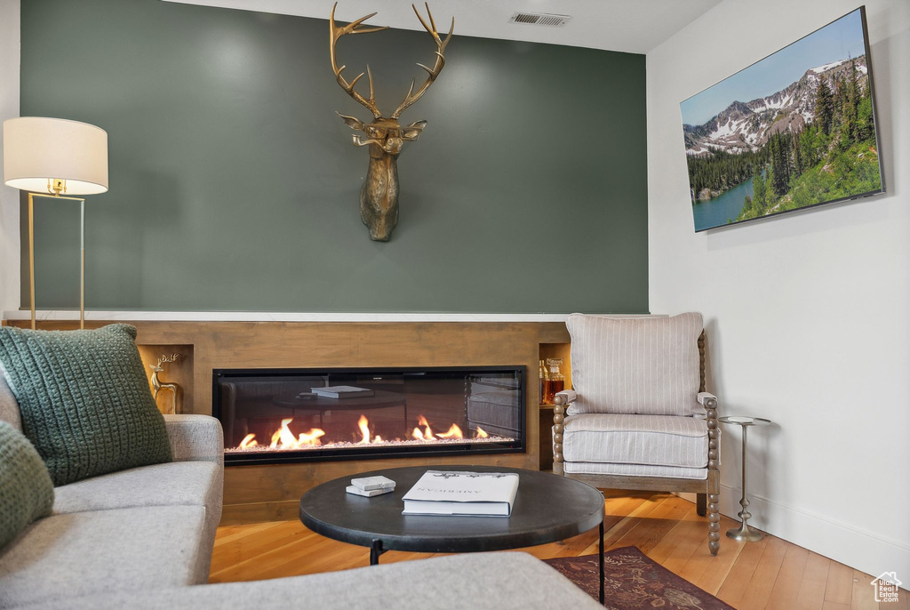 Living area featuring wood finished floors, a glass covered fireplace, and baseboards