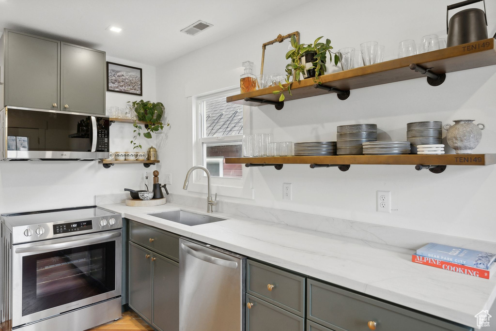 Kitchen with open shelves, appliances with stainless steel finishes, a sink, gray cabinets, and light stone counters