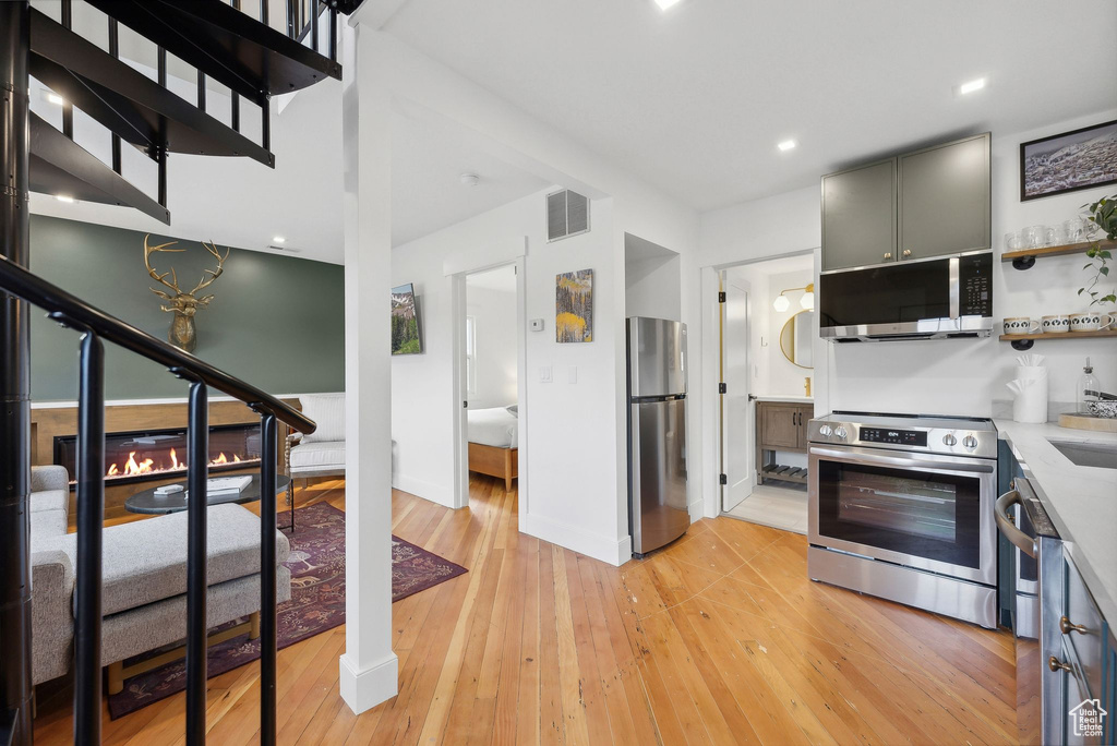 Kitchen with stainless steel appliances, light wood-style floors, open shelves, light countertops, and baseboards