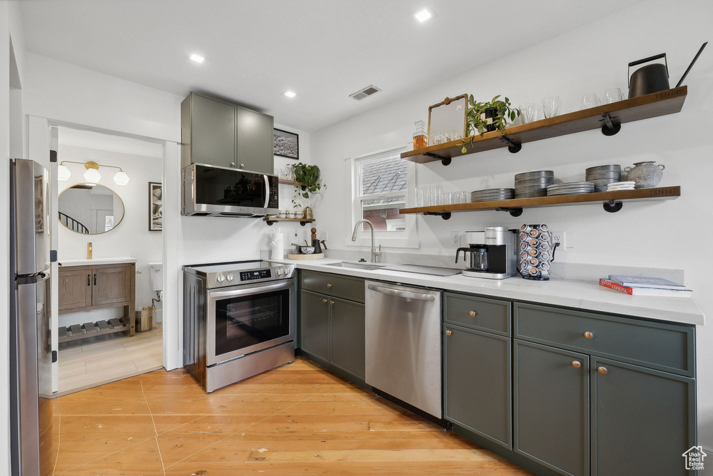 Kitchen featuring appliances with stainless steel finishes, open shelves, a sink, recessed lighting, and light countertops