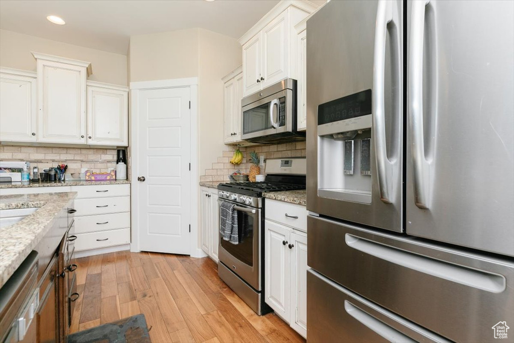 Kitchen featuring appliances with stainless steel finishes, light wood-style floors, white cabinetry, backsplash, and recessed lighting