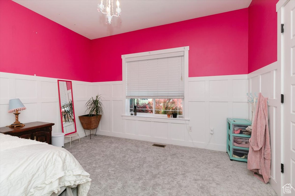 Carpeted bedroom with a decorative wall, a wainscoted wall, and a chandelier