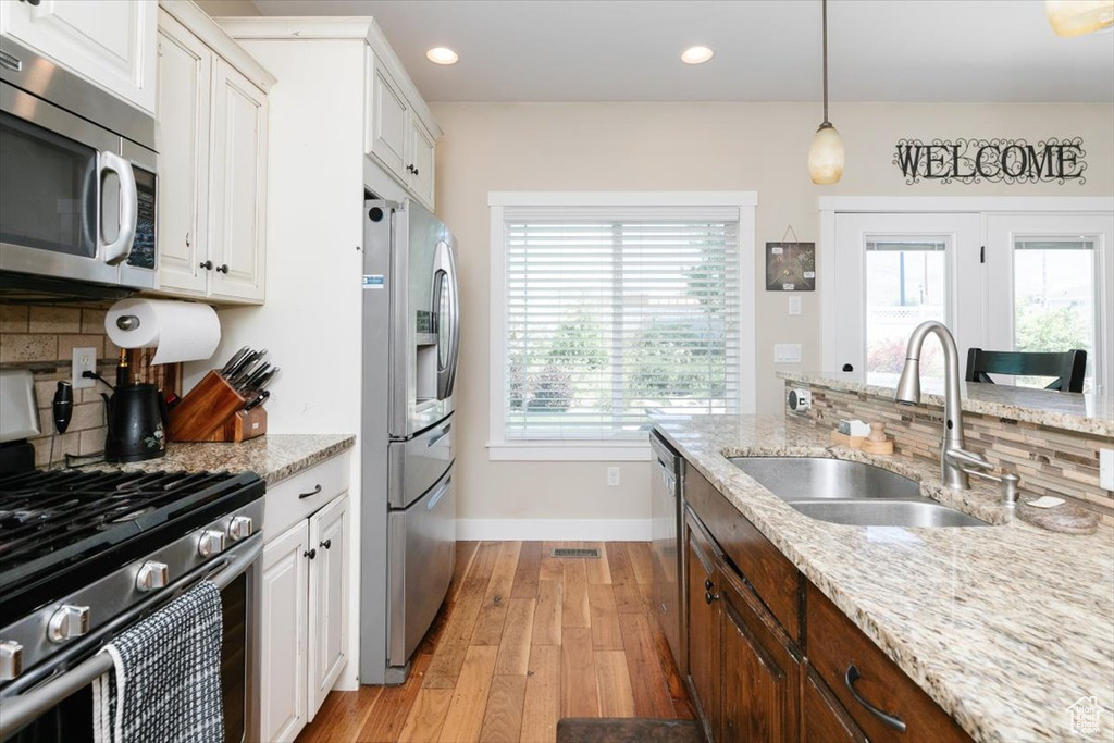 Kitchen featuring appliances with stainless steel finishes, baseboards, backsplash, light wood finished floors, and a sink