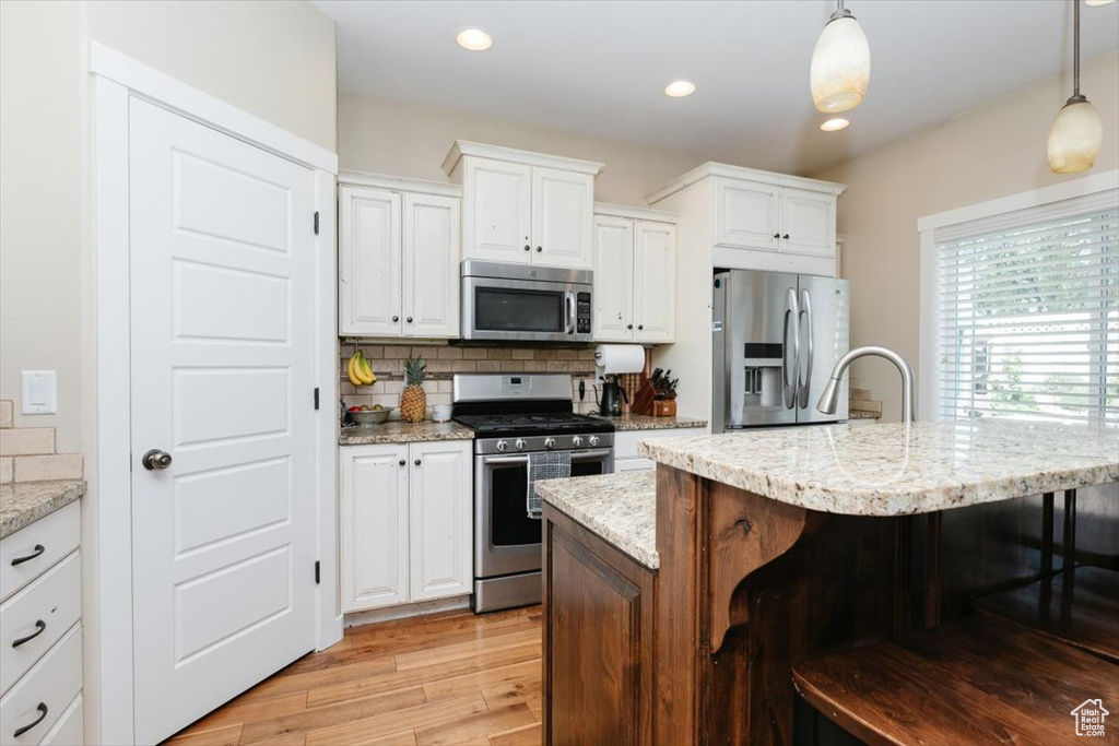 Kitchen with appliances with stainless steel finishes, a kitchen bar, white cabinetry, pendant lighting, and recessed lighting