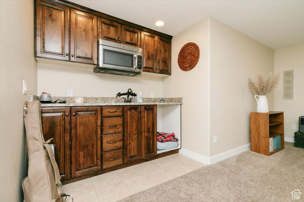 Kitchen with stainless steel microwave, baseboards, light stone countertops, and light carpet