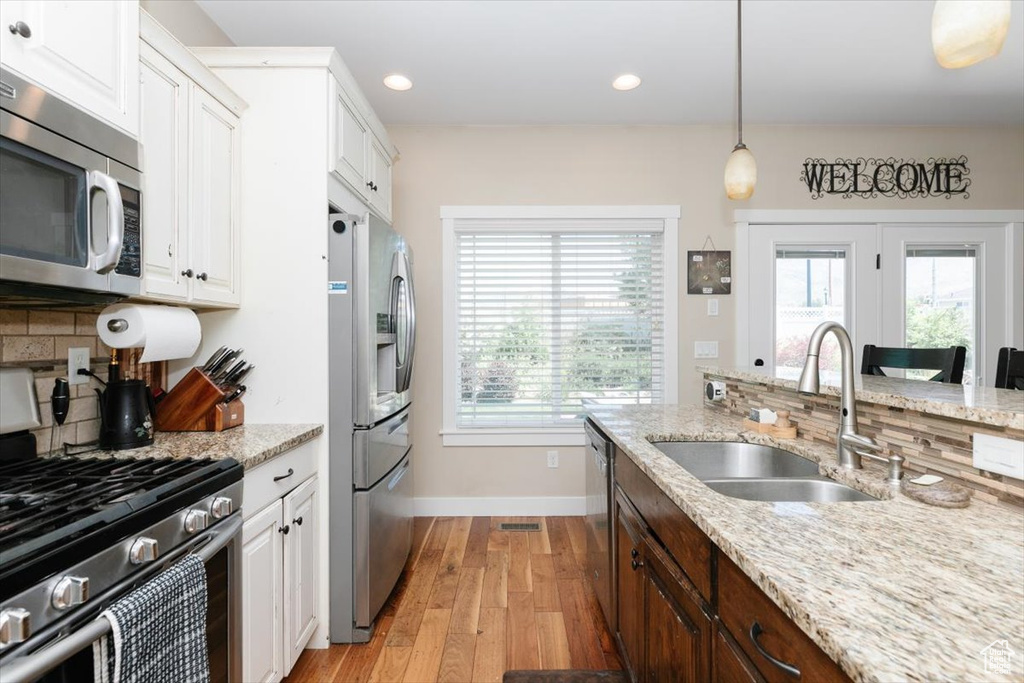 Kitchen featuring appliances with stainless steel finishes, a sink, baseboards, light wood finished floors, and backsplash