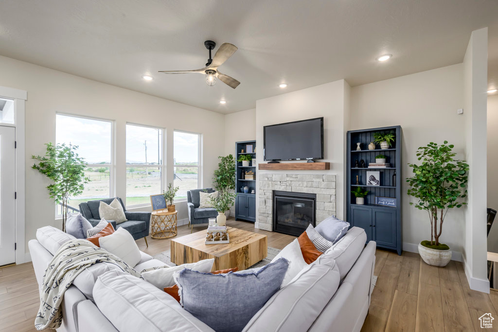 Living area with ceiling fan, a stone fireplace, light wood-style flooring, recessed lighting, and baseboards