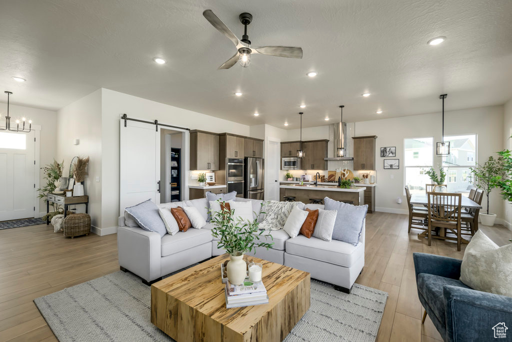 Living area with a barn door, a ceiling fan, light wood-type flooring, a chandelier, and recessed lighting