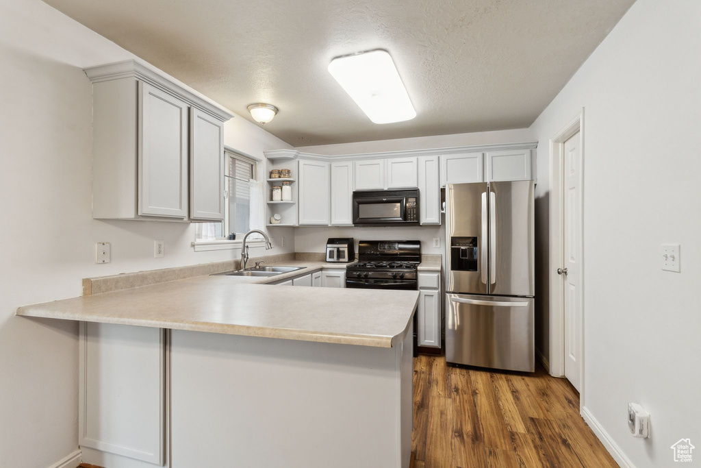Kitchen featuring black appliances, a sink, a peninsula, open shelves, and light countertops