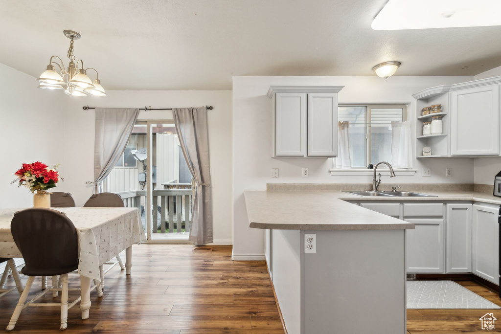Kitchen featuring a sink, a peninsula, dark wood finished floors, light countertops, and hanging light fixtures