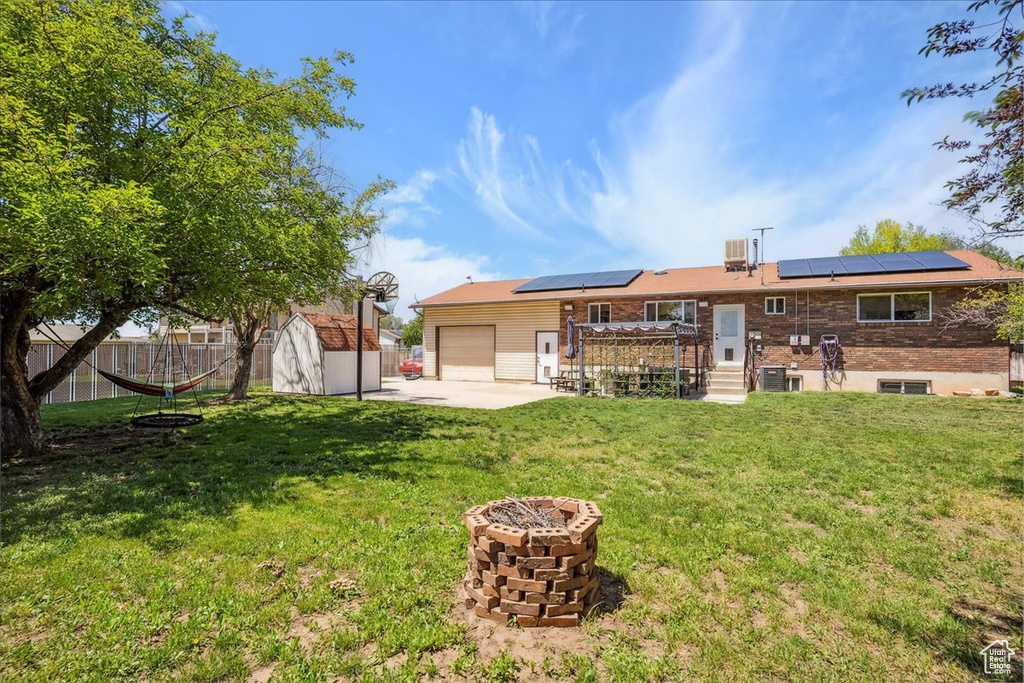 Back of house with an attached garage, a fire pit, roof mounted solar panels, and concrete driveway