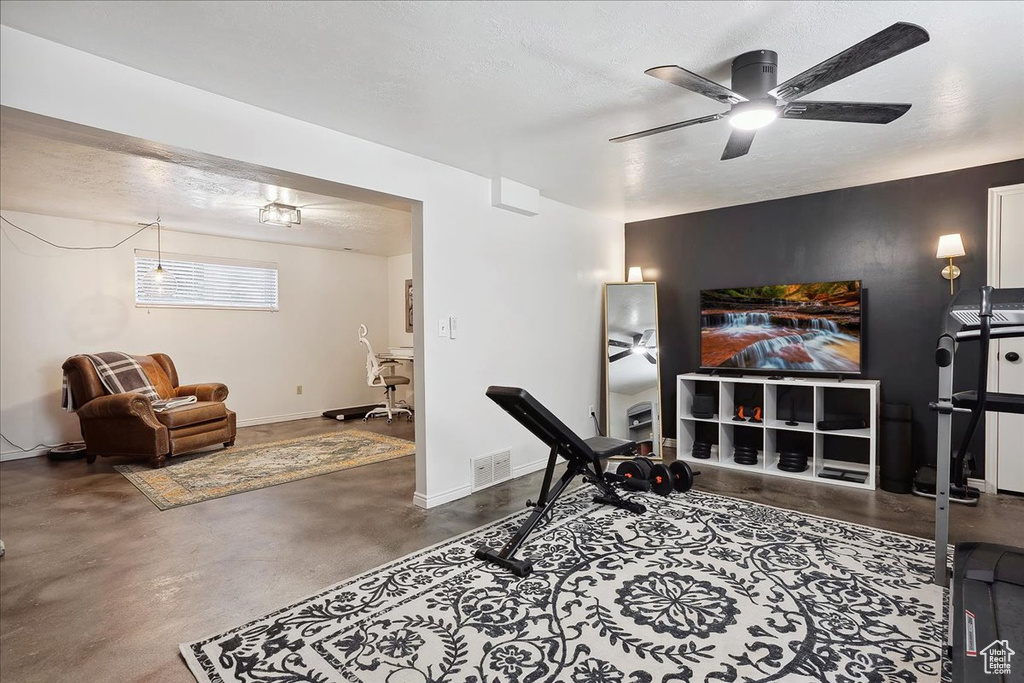 Living area featuring finished concrete floors, a ceiling fan, a textured ceiling, and baseboards