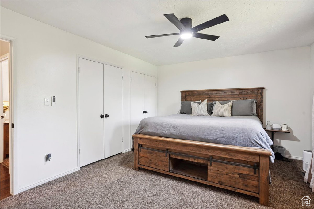 Carpeted bedroom with two closets, a ceiling fan, and baseboards