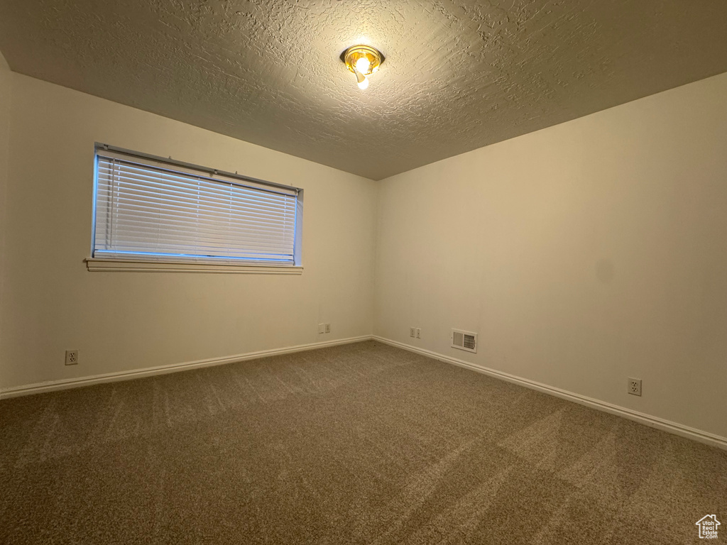 Spare room featuring dark carpet, a textured ceiling, and baseboards