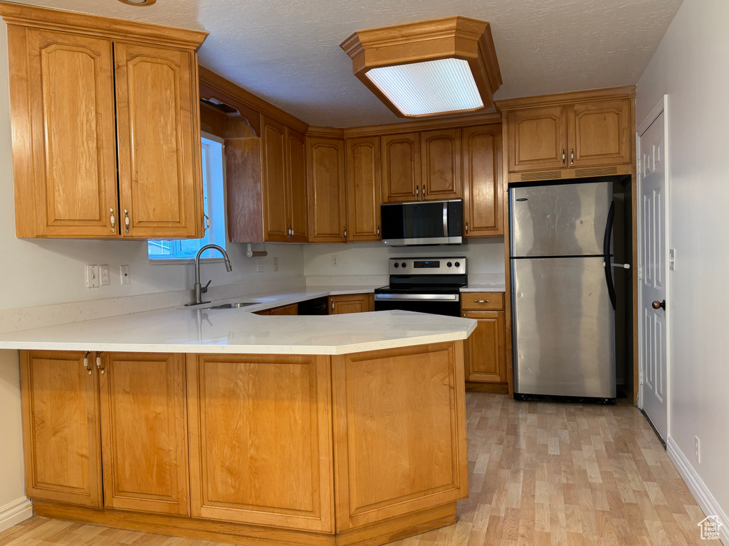 Kitchen with appliances with stainless steel finishes, a sink, a peninsula, light wood-type flooring, and light countertops