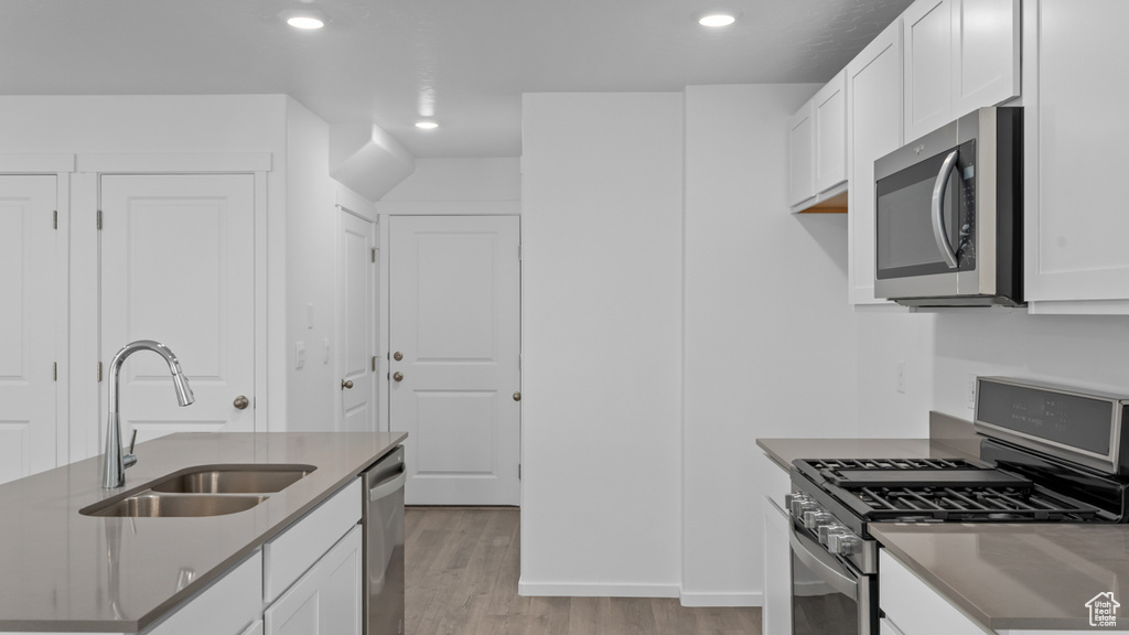 Kitchen with appliances with stainless steel finishes, a sink, light wood finished floors, recessed lighting, and white cabinets