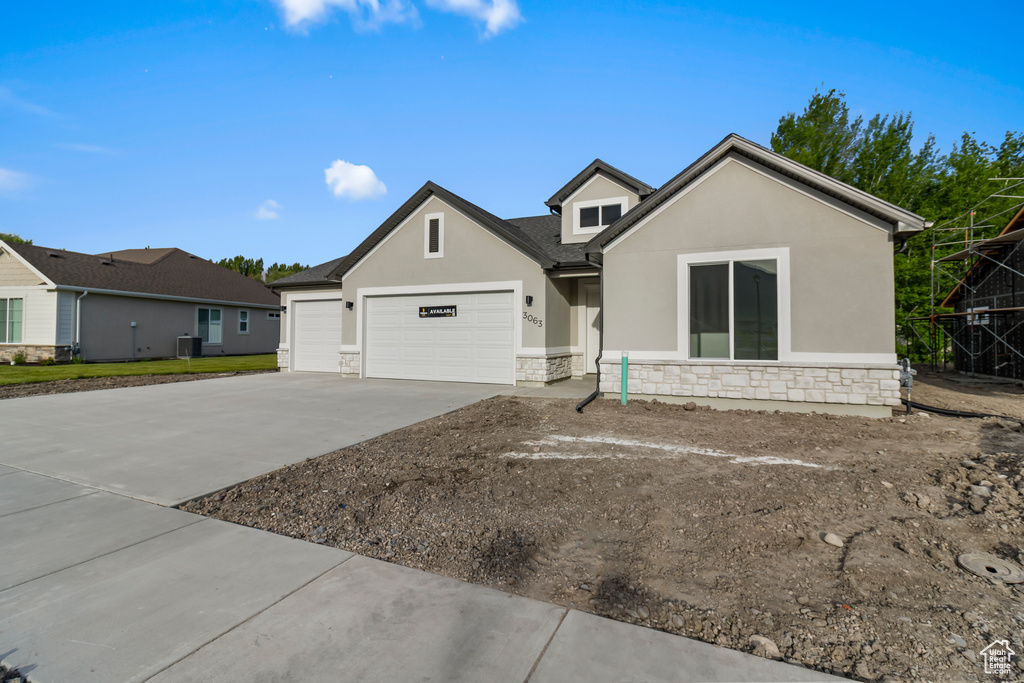 View of front of home with stone siding, stucco siding, driveway, a garage, and central air condition unit