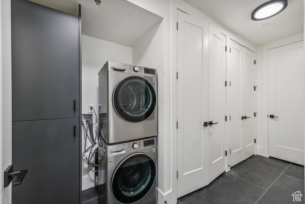 Washroom with stacked washer / dryer and dark tile patterned flooring