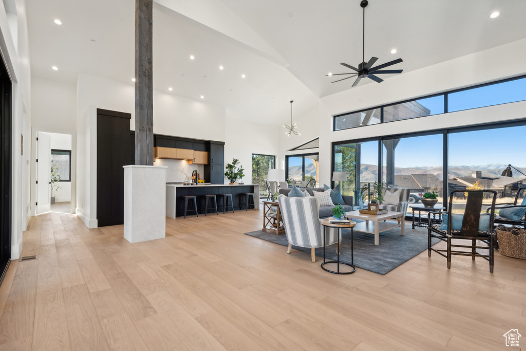 Living room with high vaulted ceiling, ceiling fan, light wood-type flooring, recessed lighting, and a chandelier