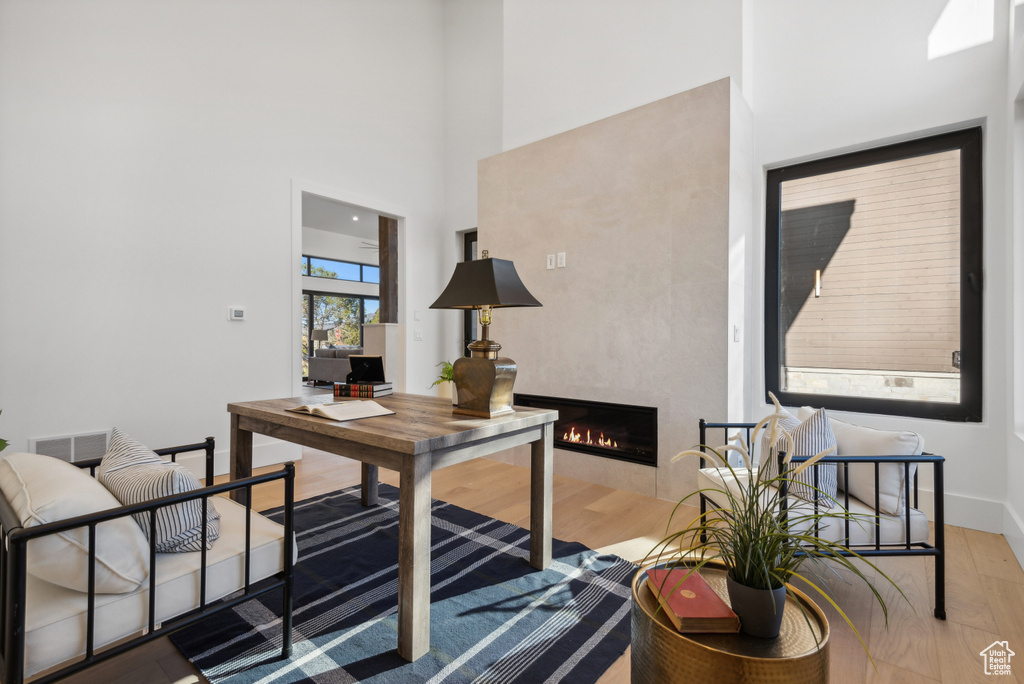Home office featuring wood finished floors, a towering ceiling, a lit fireplace, and baseboards
