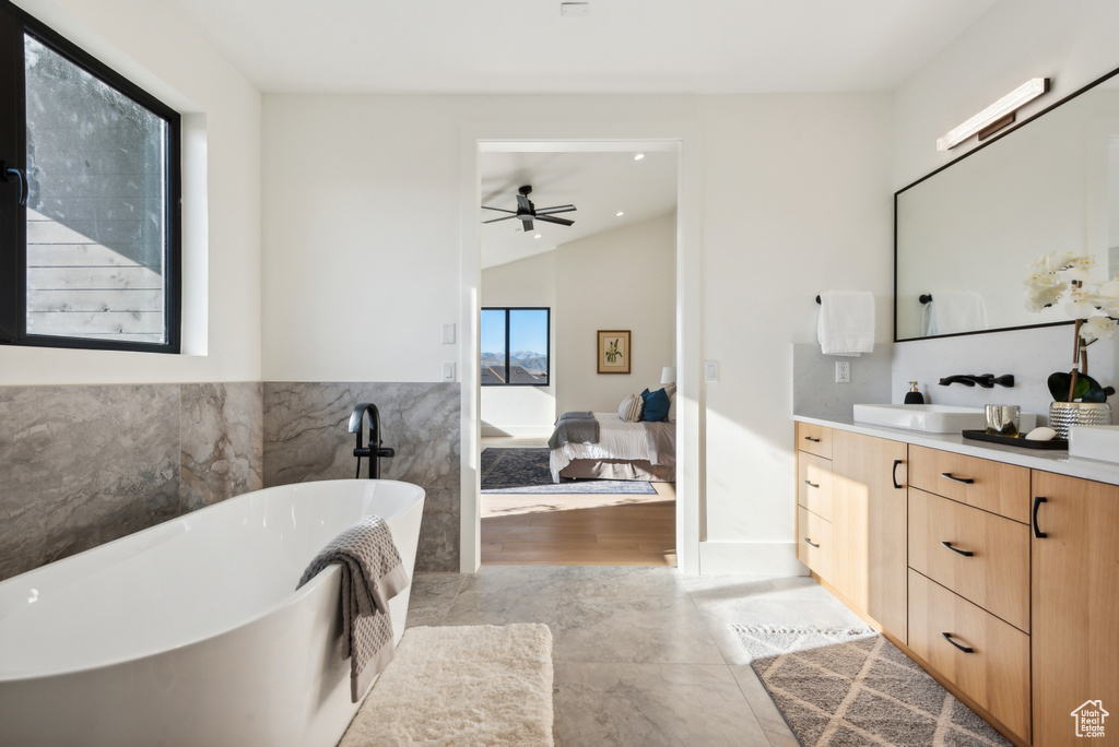 Full bathroom with vanity, a freestanding tub, ceiling fan, vaulted ceiling, and tile walls
