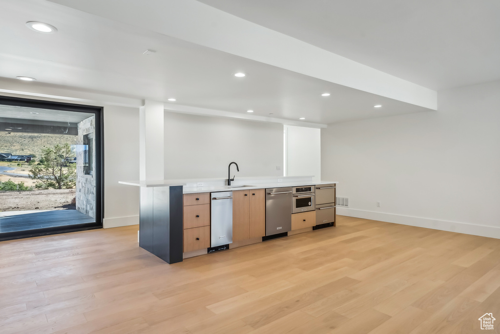 Kitchen with stainless steel appliances, light countertops, light wood-style floors, baseboards, and light brown cabinetry