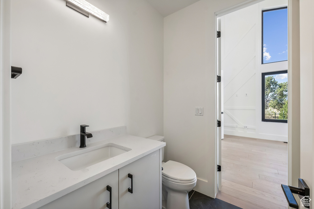 Half bathroom with toilet, vanity, and wood finished floors