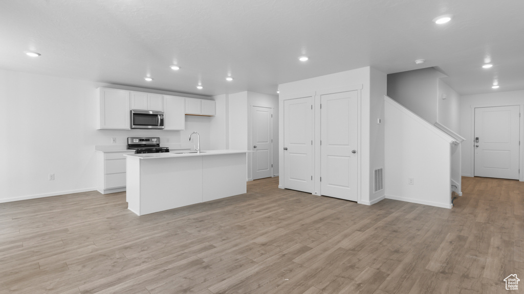 Kitchen featuring appliances with stainless steel finishes, white cabinetry, recessed lighting, baseboards, and a center island with sink