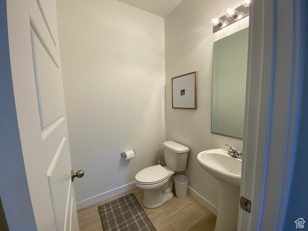 Half bathroom featuring wood finished floors, toilet, baseboards, and a sink