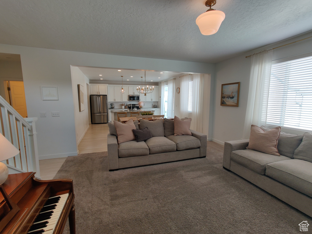 Living room with a chandelier, baseboards, a textured ceiling, stairs, and light carpet