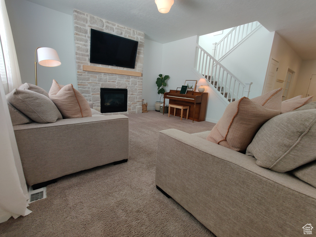 Carpeted living room featuring a stone fireplace, stairs, and baseboards