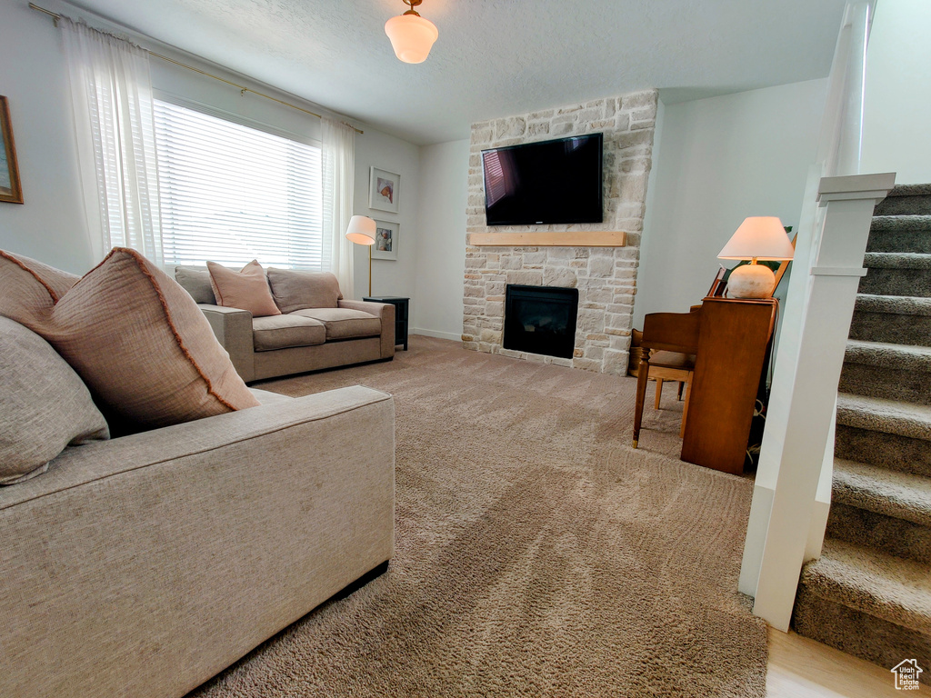 Carpeted living room with stairs, a fireplace, and a textured ceiling