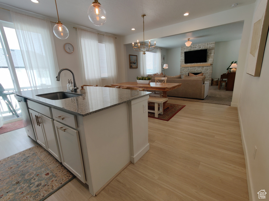 Kitchen with a sink, a stone fireplace, light wood-style flooring, a center island with sink, and hanging light fixtures