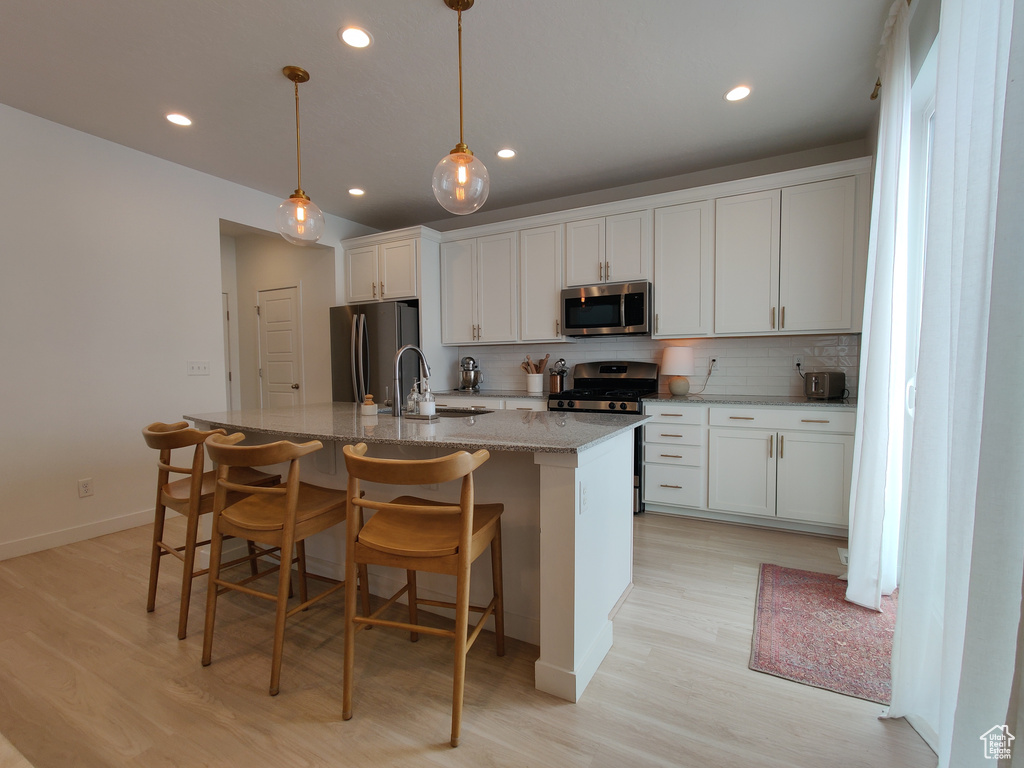 Kitchen with appliances with stainless steel finishes, light wood-style flooring, a kitchen island with sink, tasteful backsplash, and recessed lighting