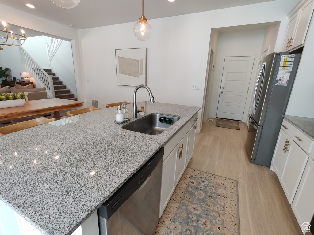Kitchen featuring stainless steel appliances, a sink, light wood-style flooring, white cabinetry, and a center island with sink