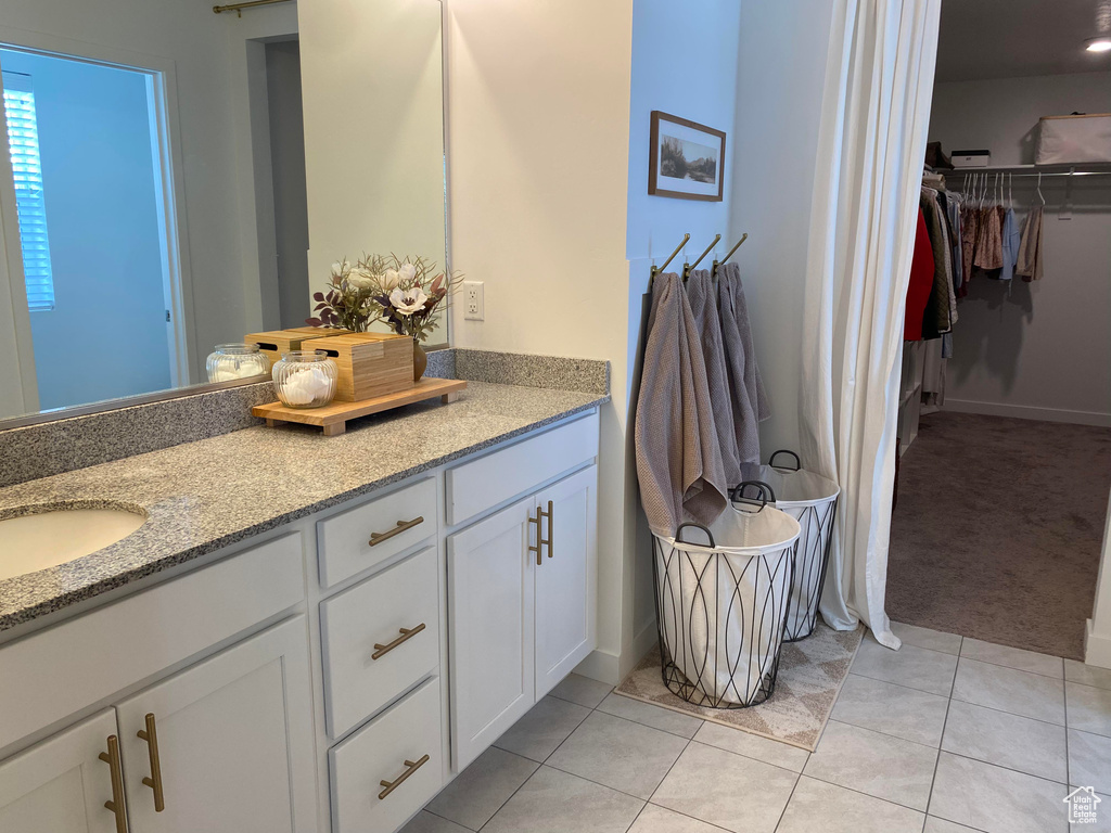 Bathroom featuring double vanity, a walk in closet, tile patterned floors, and baseboards