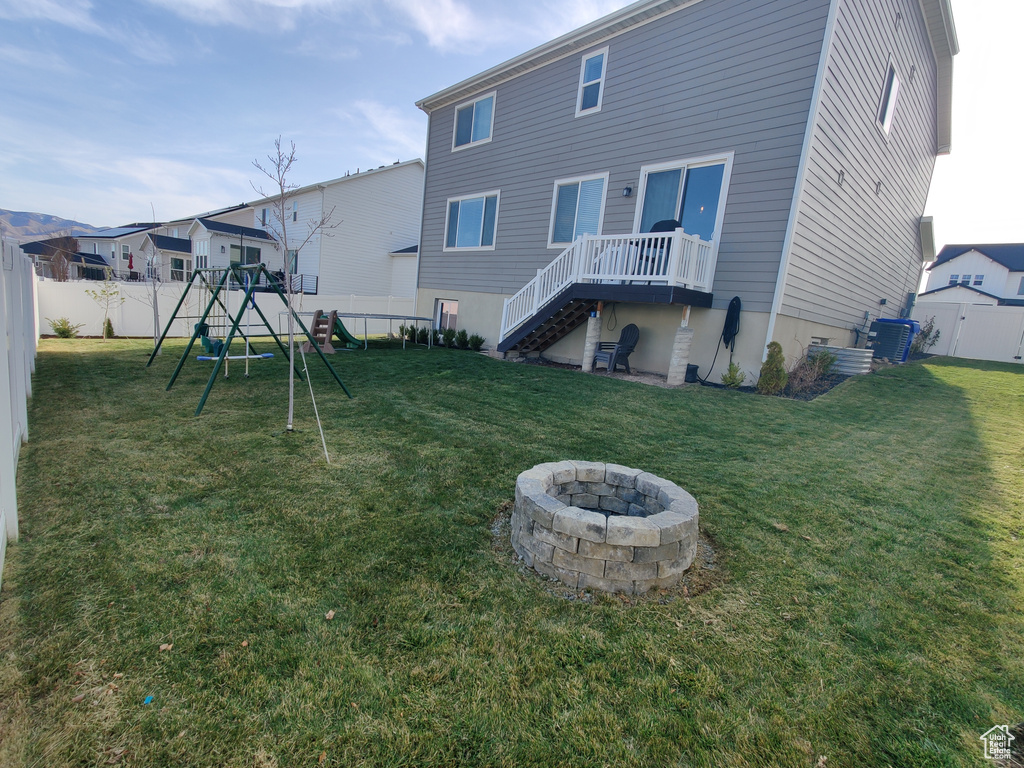 Rear view of house featuring a playground, a fire pit, stairs, and cooling unit