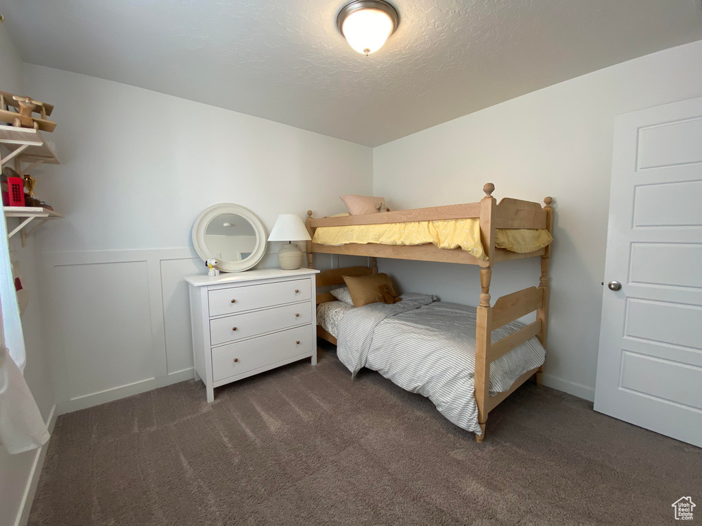 Bedroom featuring dark colored carpet, a wainscoted wall, and a textured ceiling