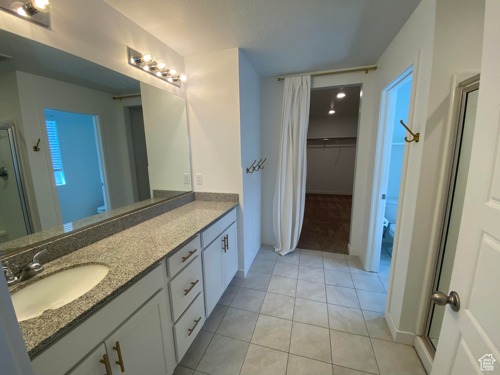Bathroom featuring toilet, double vanity, tile patterned floors, a walk in closet, and baseboards