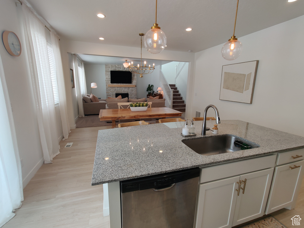 Kitchen featuring dishwasher, a sink, a large fireplace, a center island with sink, and light wood-style flooring