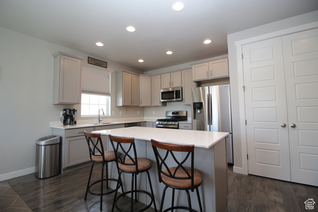 Kitchen with stainless steel appliances, a sink, a breakfast bar, dark wood finished floors, and recessed lighting
