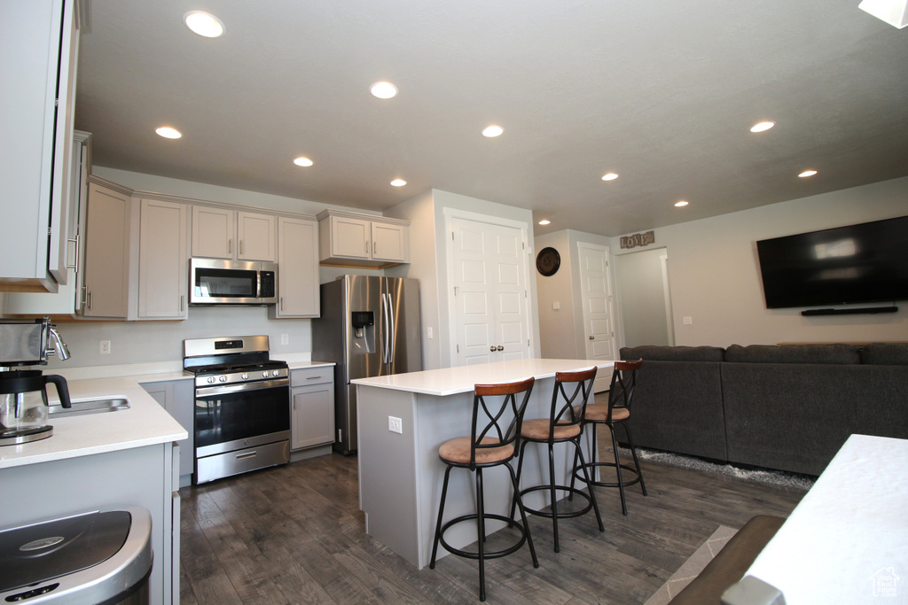 Kitchen featuring stainless steel appliances, dark wood finished floors, a kitchen bar, a center island, and recessed lighting