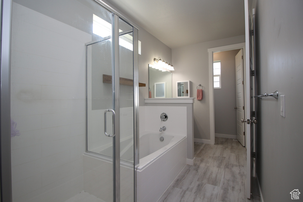 Bathroom with a stall shower, a bath, wood finished floors, and baseboards