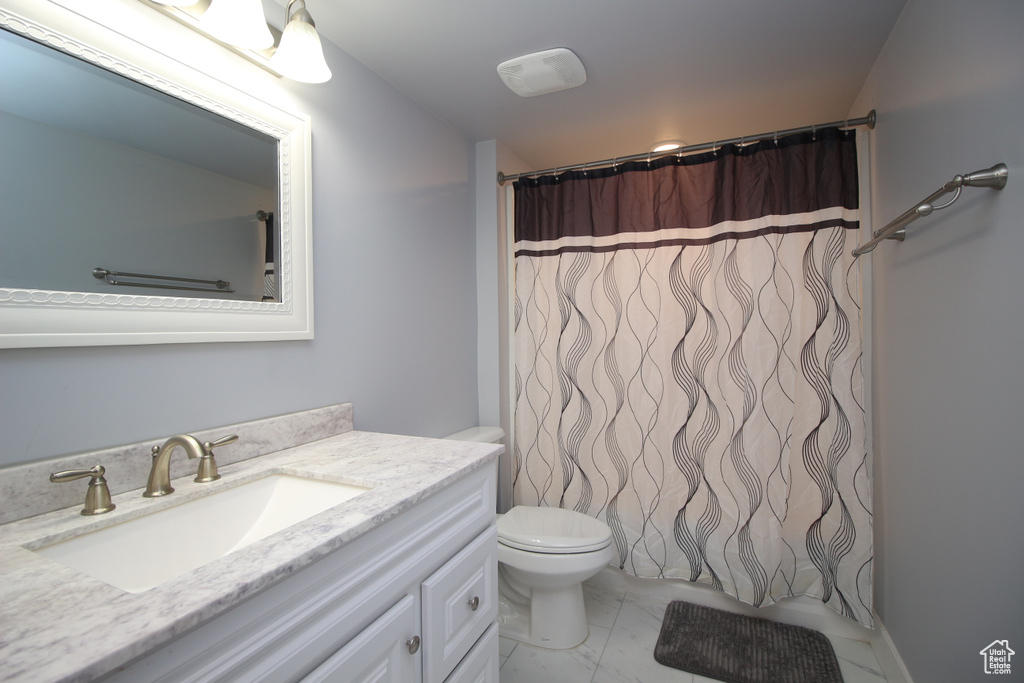 Bathroom with vanity, toilet, marble look tiles, and a shower with shower curtain