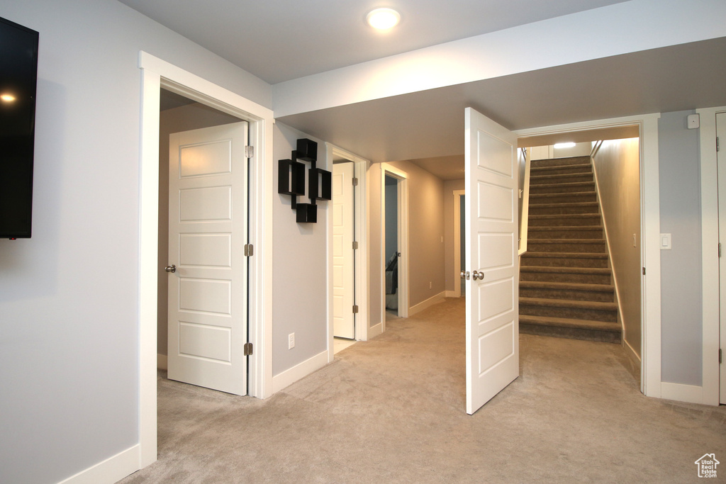 Below grade area featuring light carpet, stairway, and baseboards