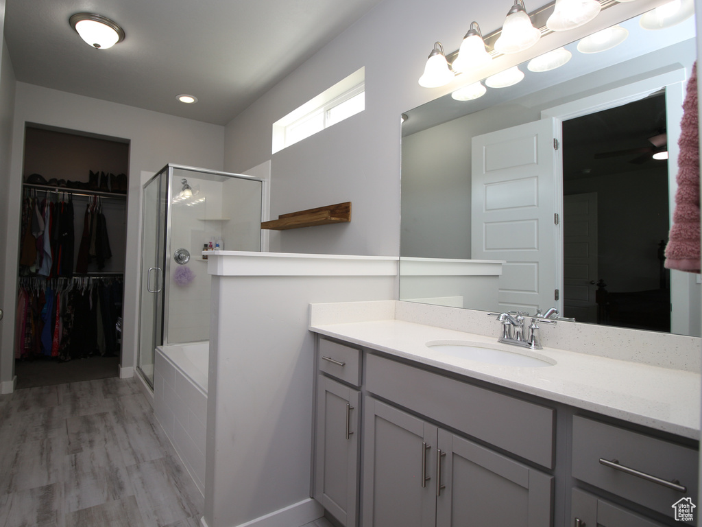 Full bath with an enclosed shower, vanity, a spacious closet, and wood finished floors
